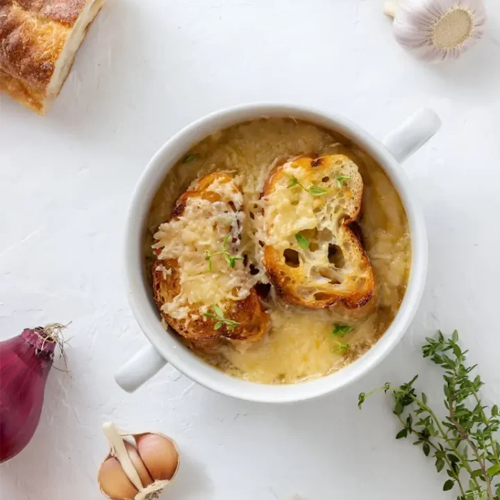 Soupe à l'oignon gratinée accompagnée de pain à l'ail, servie dans un bol en céramique