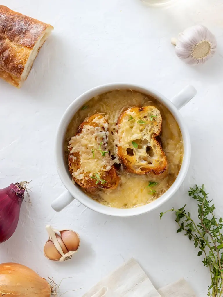 Soupe à l'oignon gratinée accompagnée de pain à l'ail, servie dans un bol en céramique