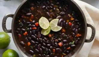 Un bol de soupe aux haricots noirs garni de quartiers de citron vert frais et de coriandre, présentant une couleur riche et sombre et des garnitures vibrantes