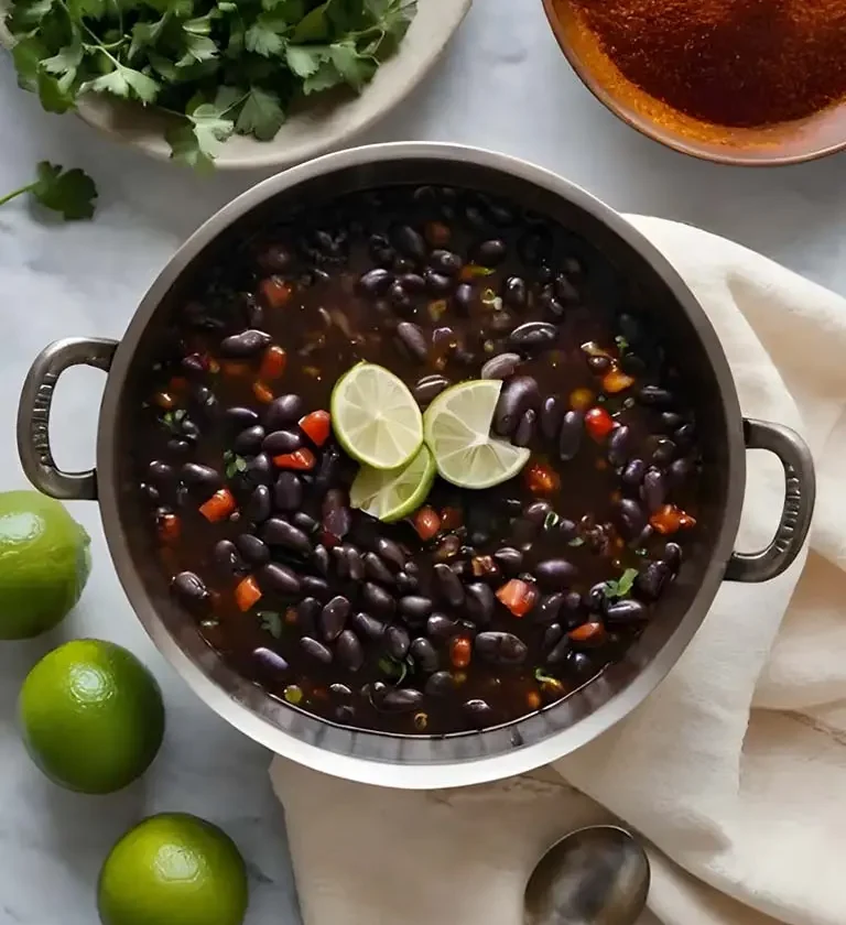 Un bol de soupe aux haricots noirs garni de quartiers de citron vert frais et de coriandre, présentant une couleur riche et sombre et des garnitures vibrantes