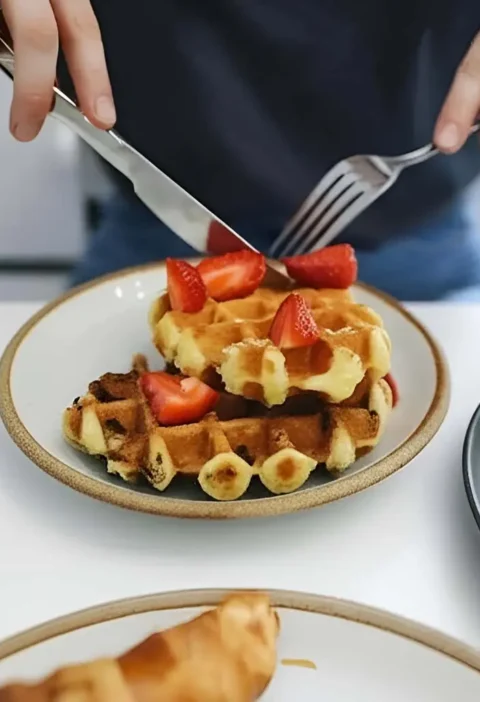 Une personne coupe une gaufre garnie de fraises, illustrant une recette de gaufres délicieuse et appétissante