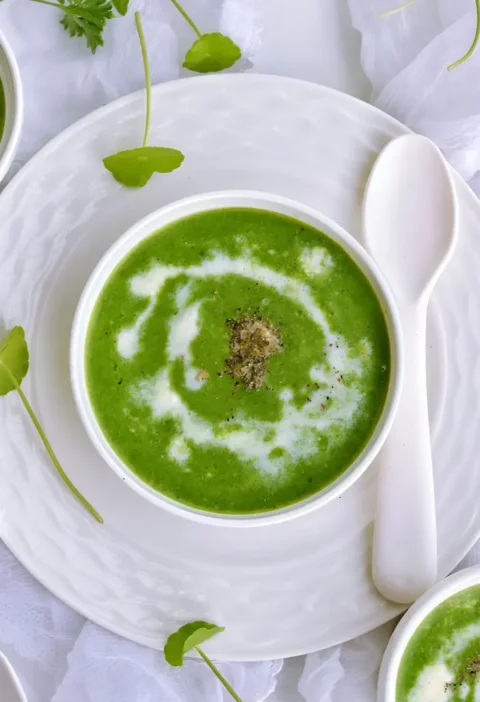 Un bol de velouté de cresson aux pommes de terre avec une cuillère et deux autres cuillères à côté.