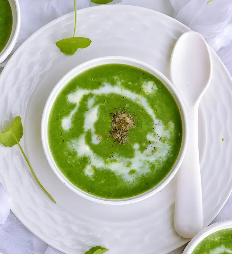Un bol de velouté de cresson aux pommes de terre avec une cuillère et deux autres cuillères à côté.