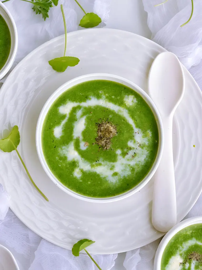 Un bol de velouté de cresson aux pommes de terre avec une cuillère et deux autres cuillères à côté.